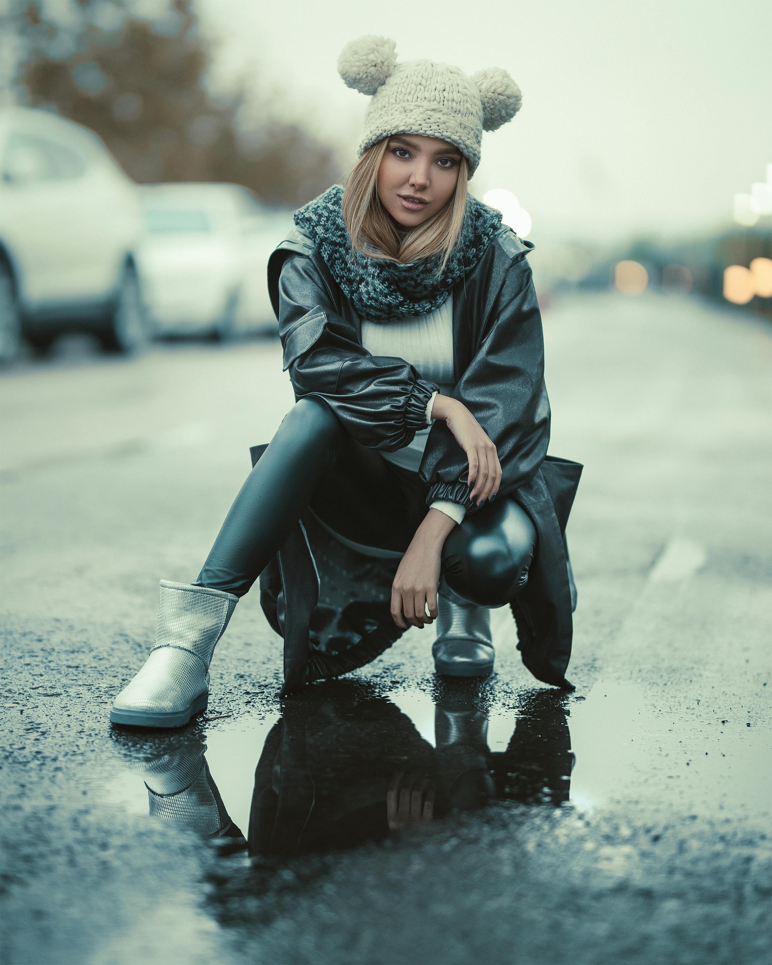 Stylish woman in winter streetwear posing outdoors on a wet street.